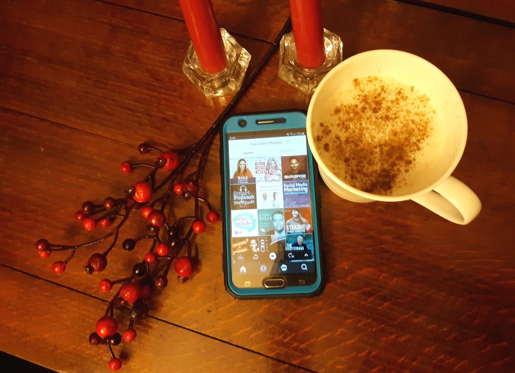 A cup of eggnog, a cellphone with a podcast app open, red candles on a table.